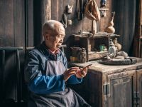 Chinese Senior Man Tapping On Mobile In Wooden House