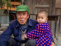 Little Boy Hugging His Grandfather On Rural Street, Guizhou, China.